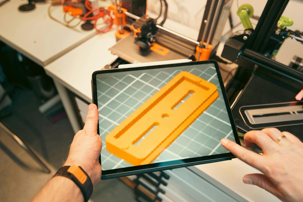 Un profesional utiliza una tablet para visualizar un prototipo de modelo 3D en un taller equipado con impresoras 3D y piezas artísticas.